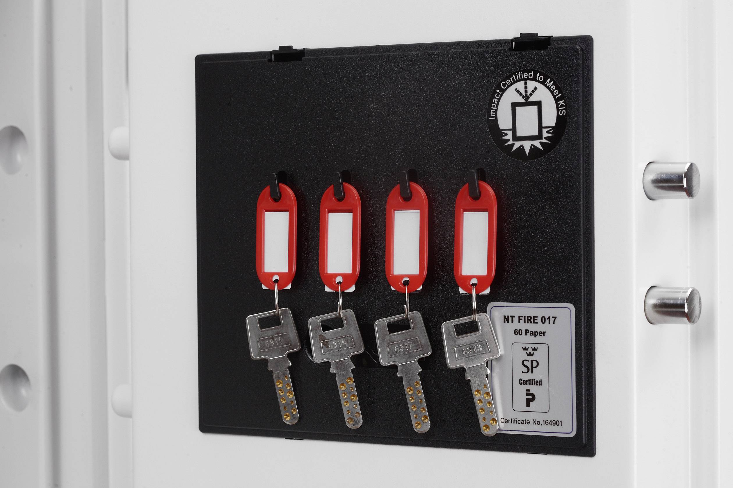 Four keys with red tags are hanging on a black board attached to a white surface.