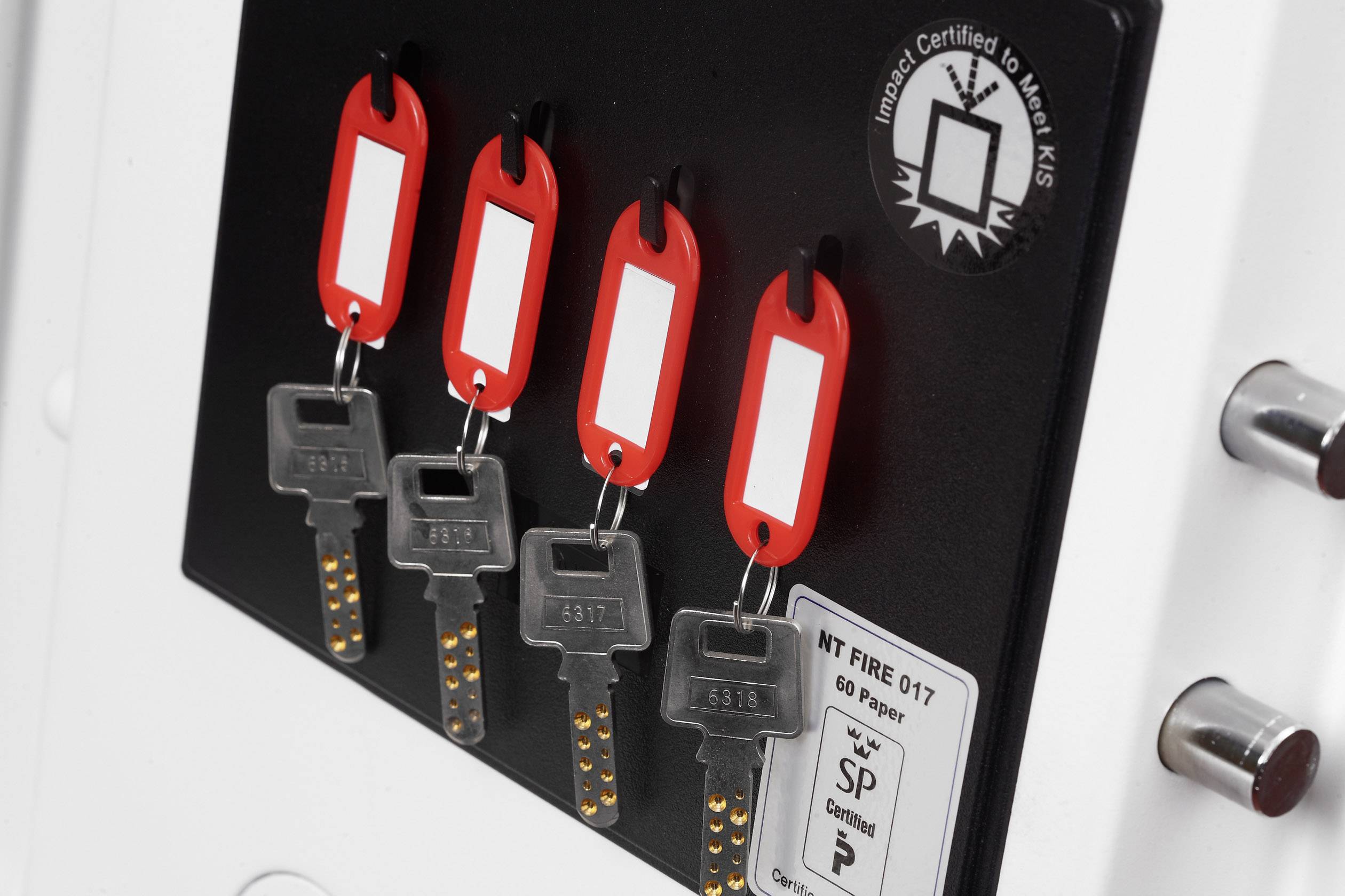 Four identical keys hang from red tags against a black background. A certification label is visible.