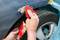 A person is repairing a car body, applying body filler to a wheel arch with red filler, in order to repair damage.
