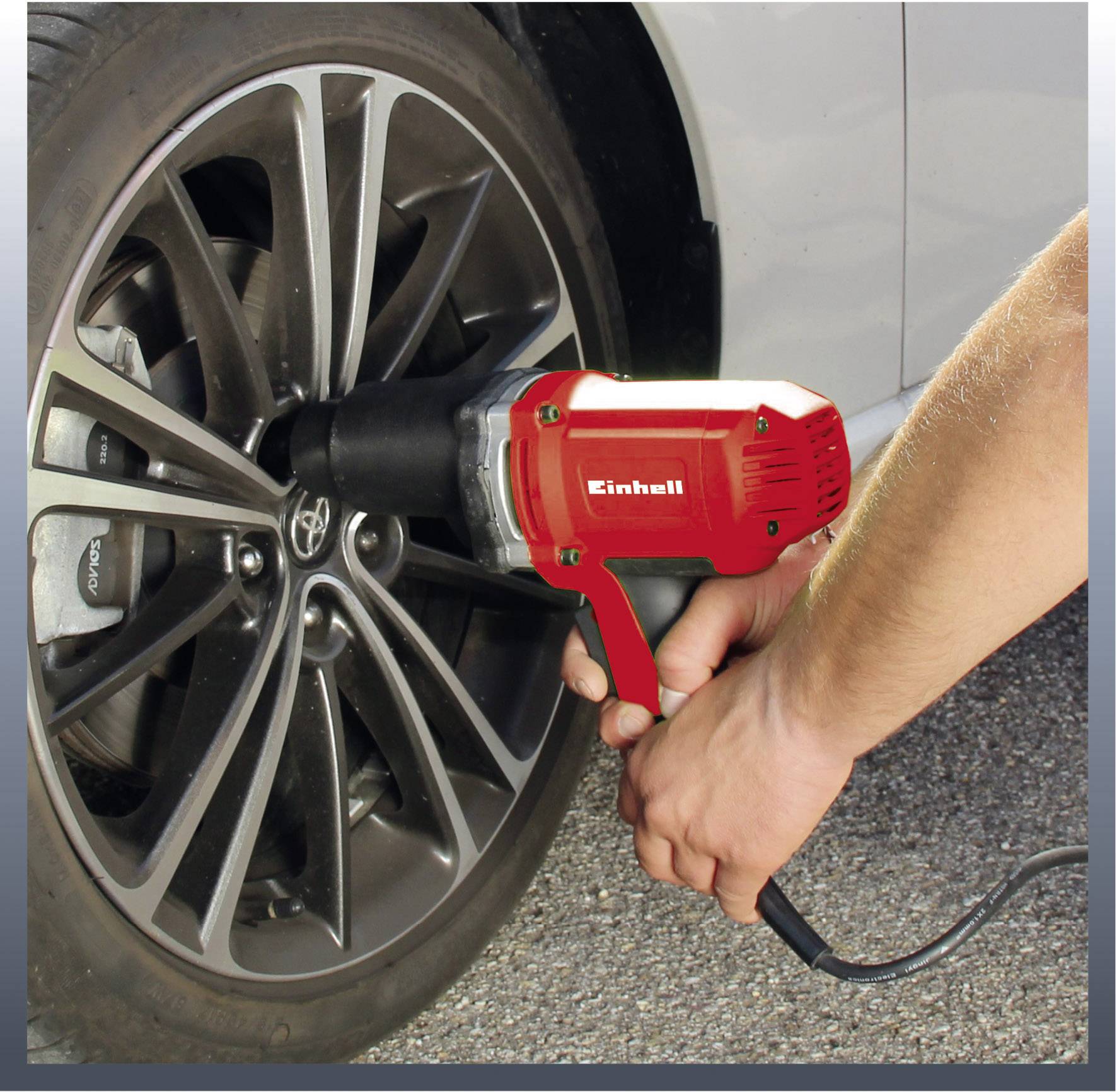 A person is using a red electric screwdriver to change the wheel of a silver car.