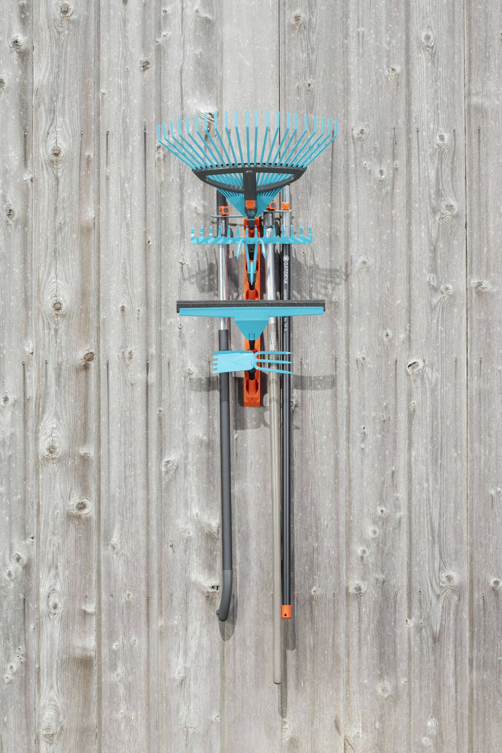 A blue and orange rake hangs on a vertical wooden lath wall.