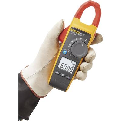 A digital clamp multimeter is being held in a gloved hand, displaying '600.0' on the screen.