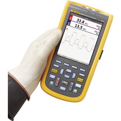 A hand is holding a portable measuring device with a screen displaying voltage and frequency. Main reading: 33.8 V at 13.5 Hz.