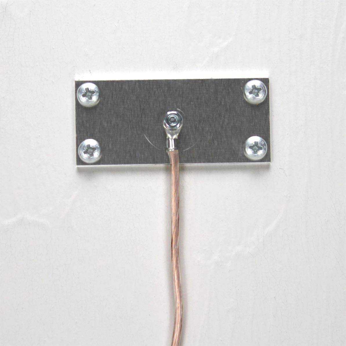 Metal plate with a wire attached in the centre, screwed to a white wall.