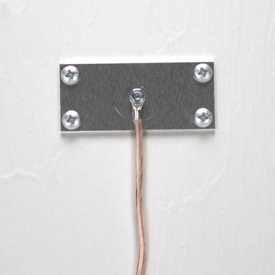 Metal plate with a wire attached in the centre, screwed to a white wall.