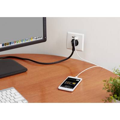 A mobile phone is connected to a power socket with a cable and is lying on a table next to an activated computer monitor.