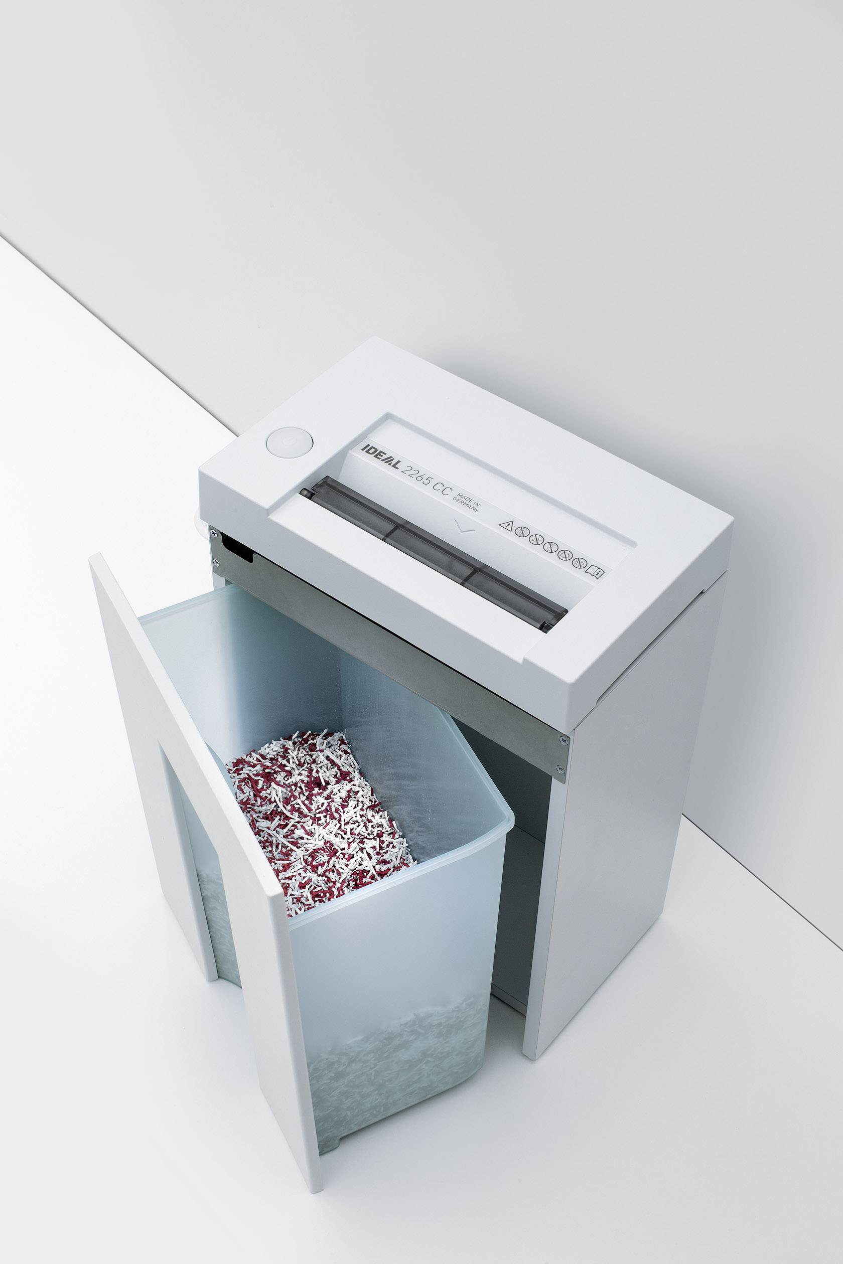 A shredder tears paper strips in a container. The device is located in a modern office environment.