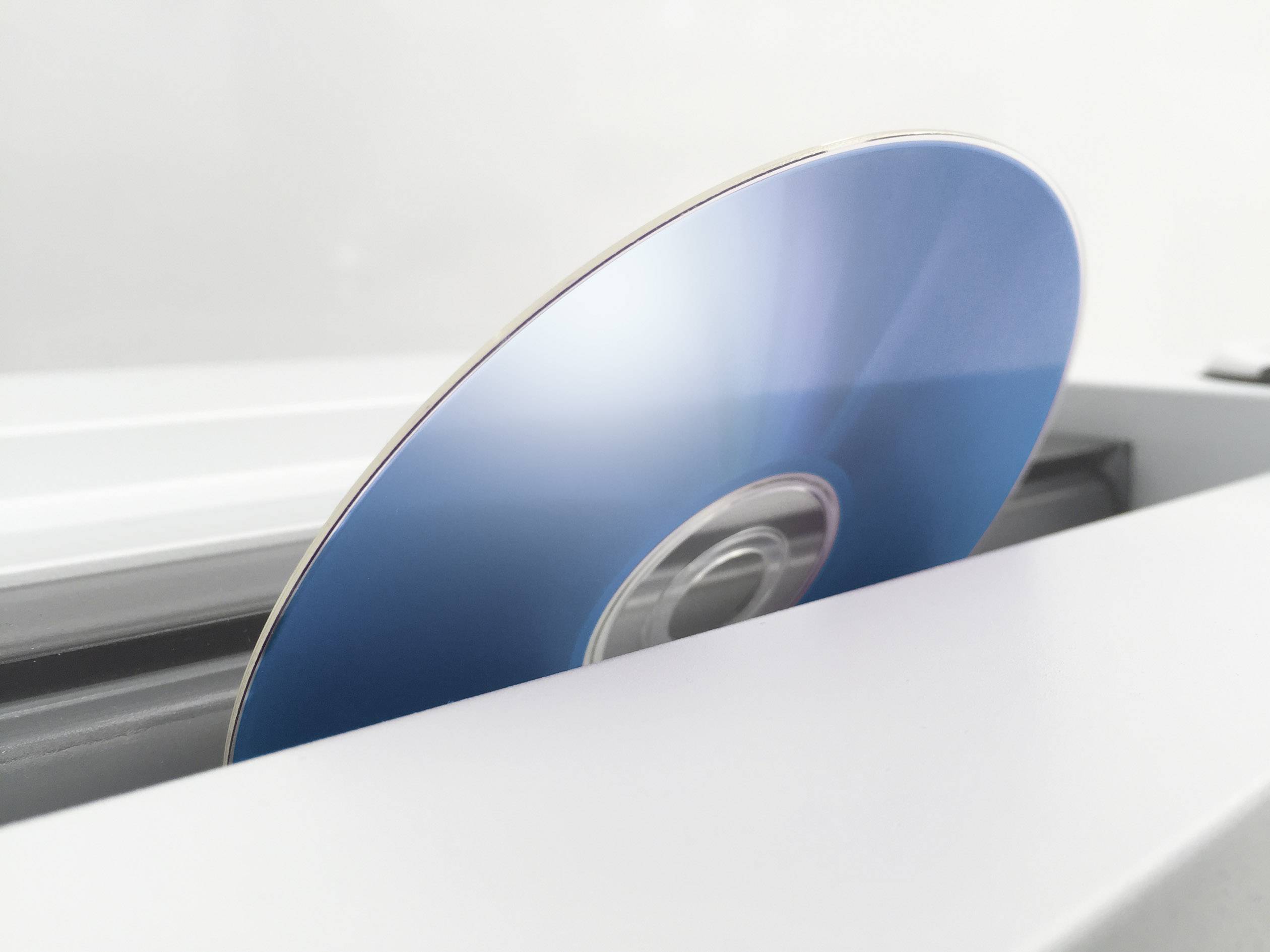 A blue disc is pushed out from a slot in a white device.