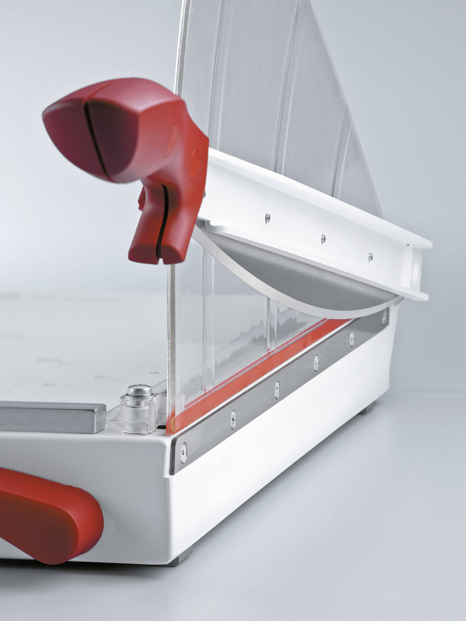 Close-up of a modern bread-slicing device with a red handle and transparent protective cover.