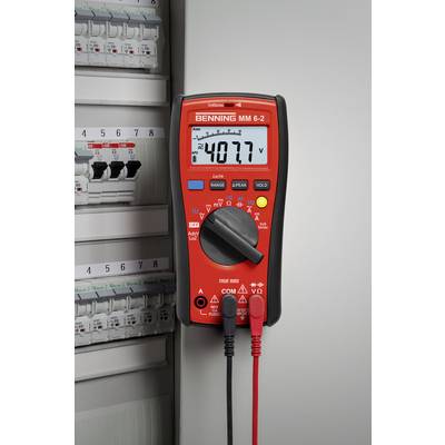 A red multimeter is displaying a voltage of 40.77 on an electronic display and is connected to an electrical control cabinet.