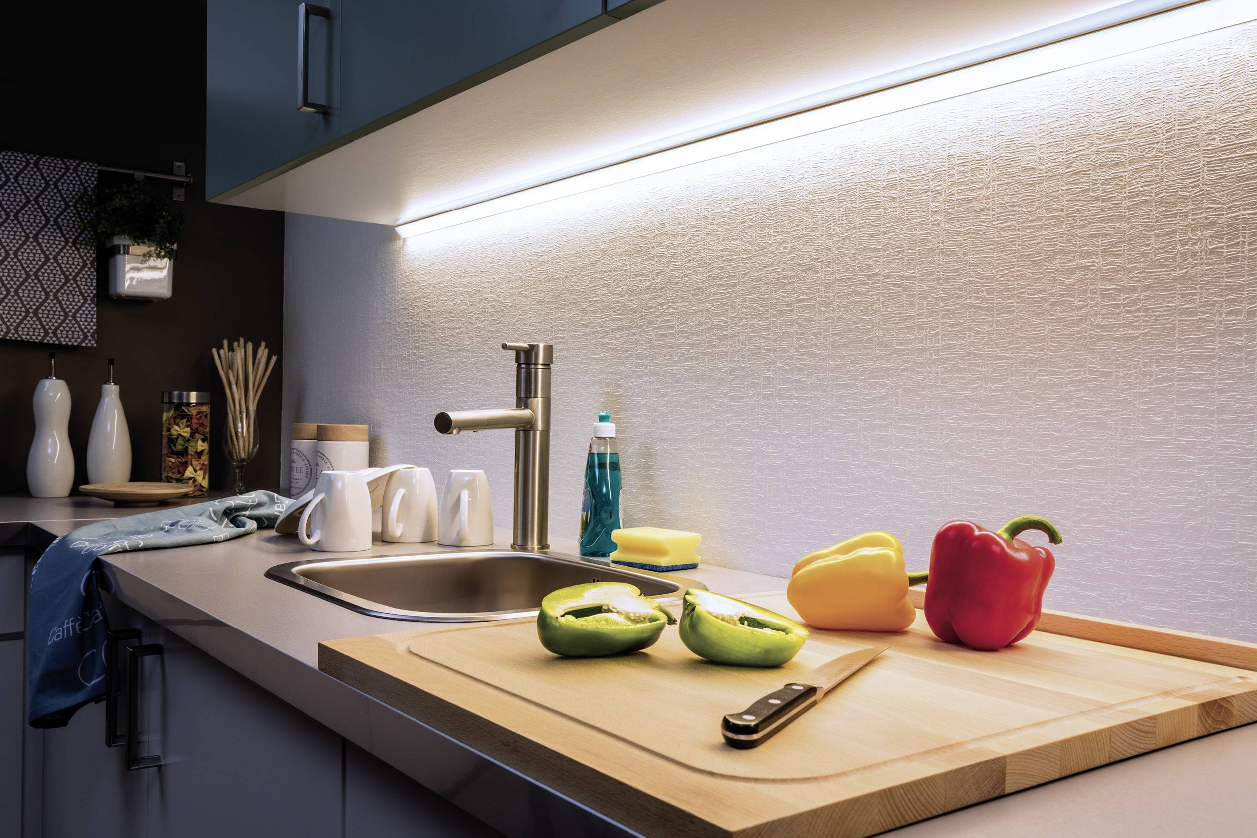 Bright kitchen with modern design. Chopping board with a green apple and peppers on the worktop beside the sink.