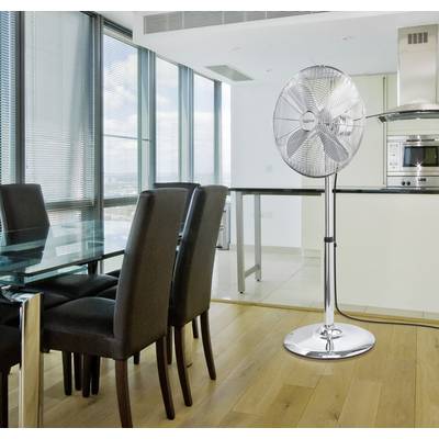 Modern dining area with a glass table and black chairs, adjacent to an open-plan kitchen. A silver pedestal fan in the room.