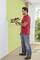 A man in a red shirt is spraying a wall green with a spray gun. He is standing in a room with large windows.