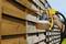 A hand sprays wood preservative onto a wooden garden fence using a spray gun on a sunny day.