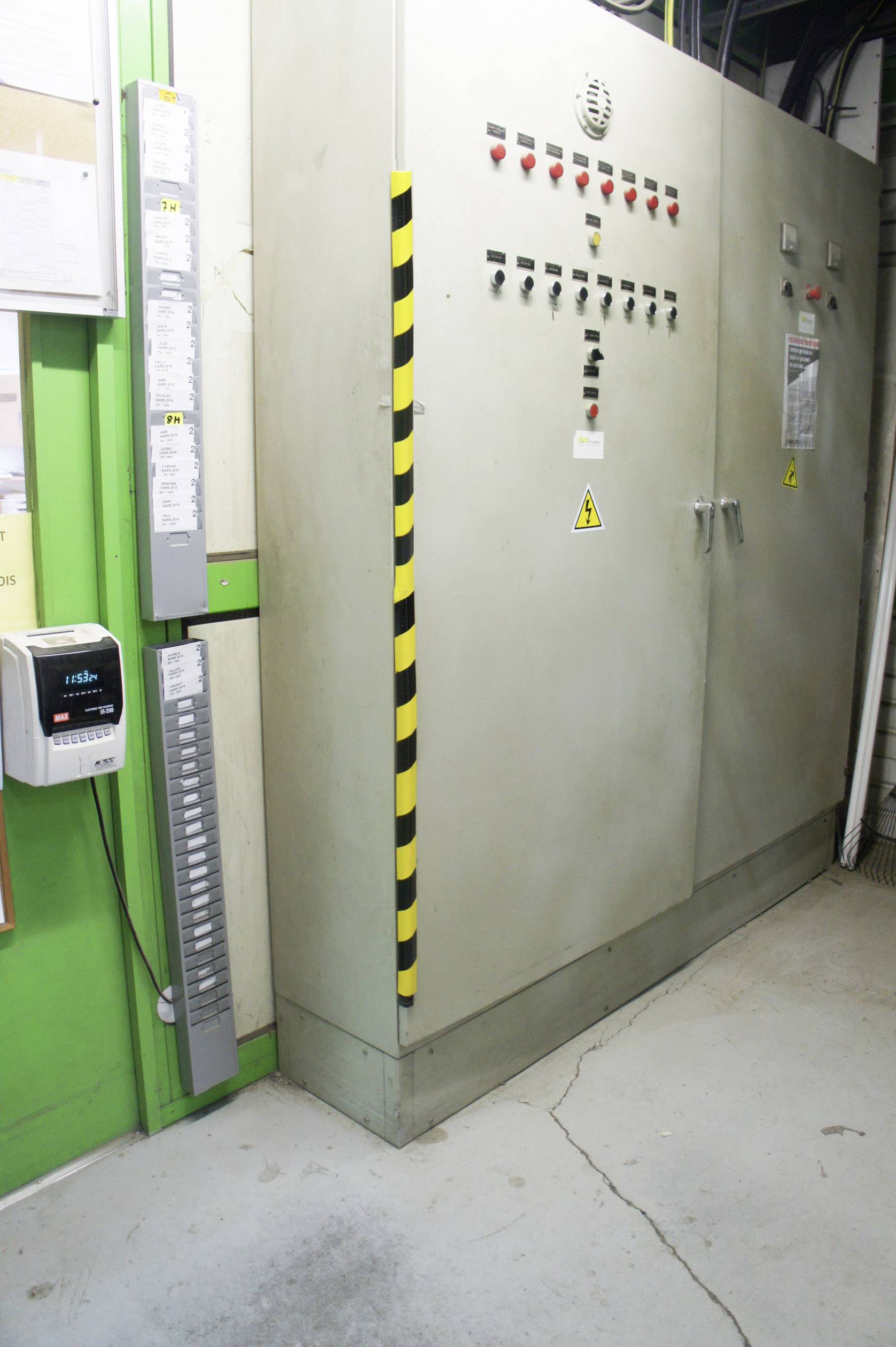 Large grey electrical cabinet in an industrial space with yellow and black warning markings; operator manuals are hanging nearby.
