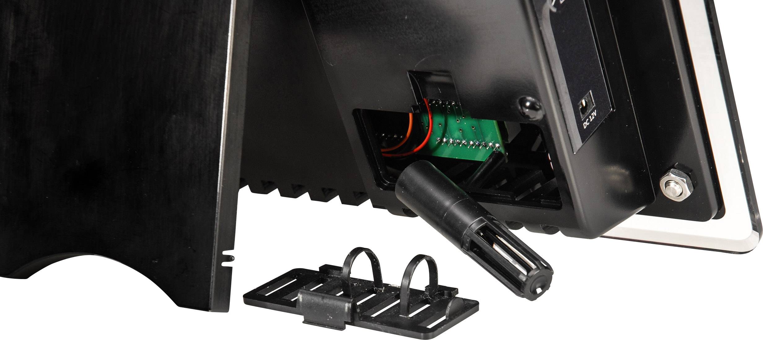 Rear view of an electronic device with its casing open. Visible cables and connections. Accessory parts are placed beside it.