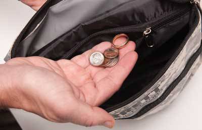 A hand is holding a few coins over an open wallet.