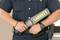A security officer is holding a hand-held metal detector branded 'GARRETT'. He is wearing a black uniform with belt accessories.