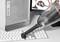 A handheld vacuum cleaner is cleaning a computer keyboard. In the background, a computer tower and two monitors are visible.