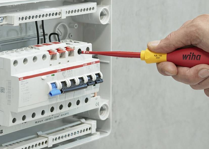 A hand is using a screwdriver to fasten or remove a fuse in an open fuse box.