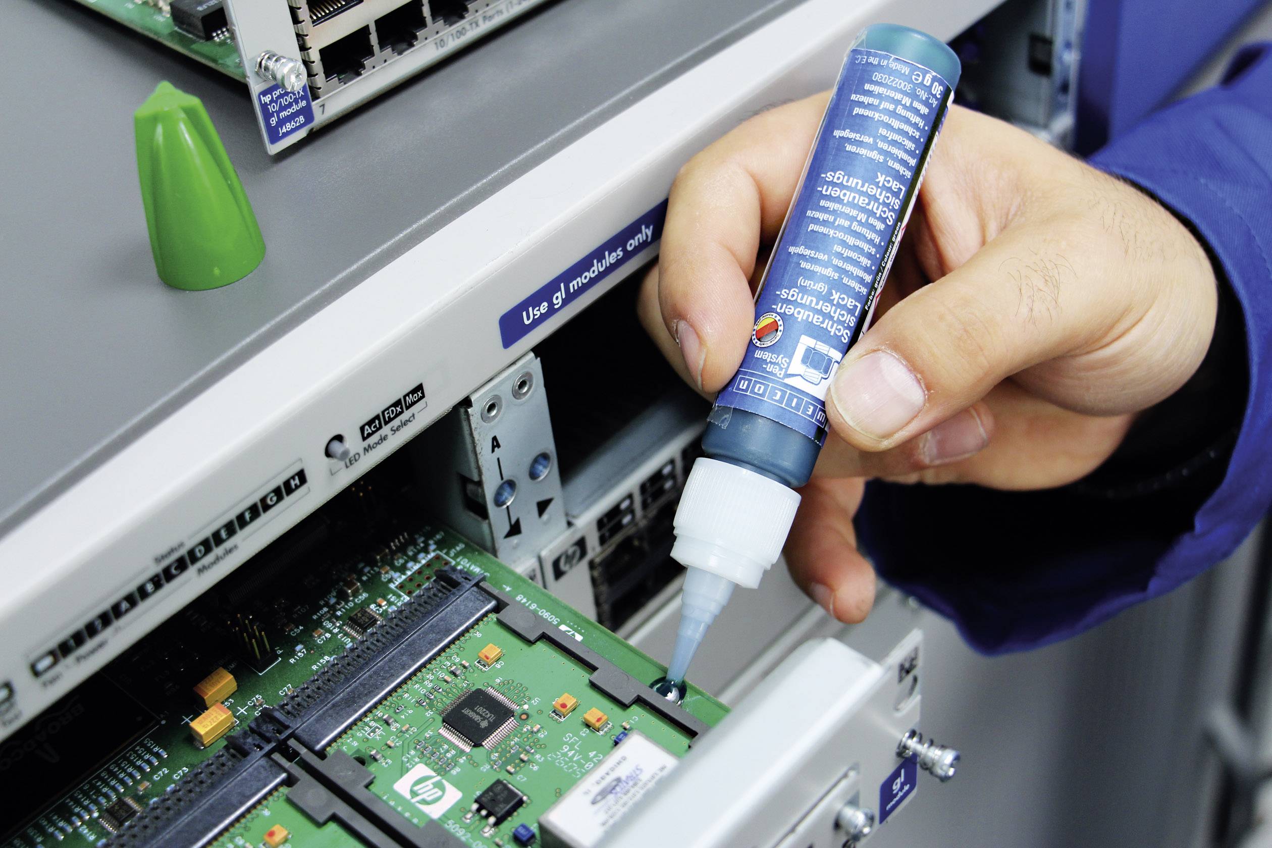 A person is applying a substance to a circuit board in a server room using a blue bottle.