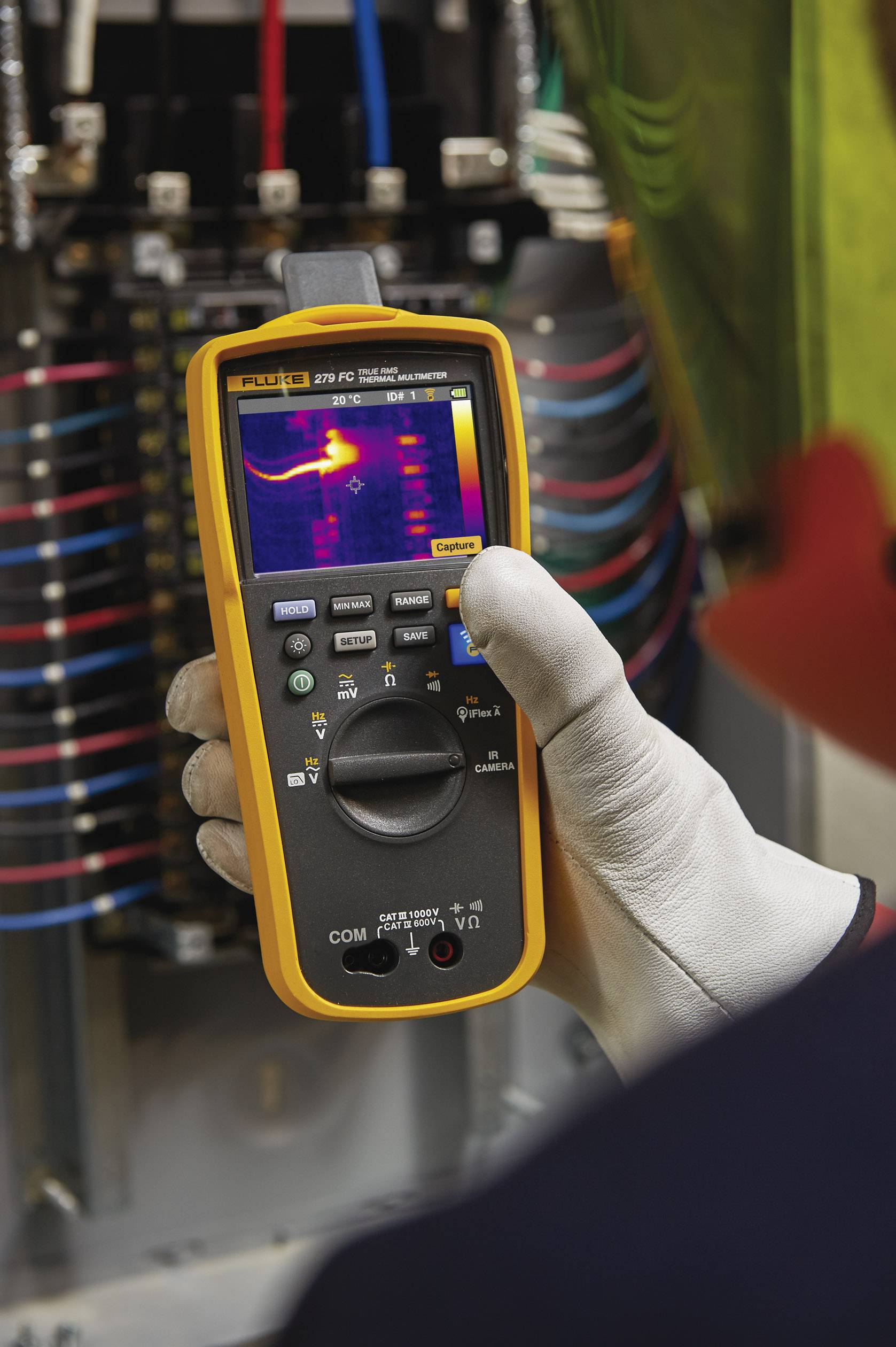 A person is using a digital multimeter with thermal imaging capability to inspect electrical components in a control cabinet.