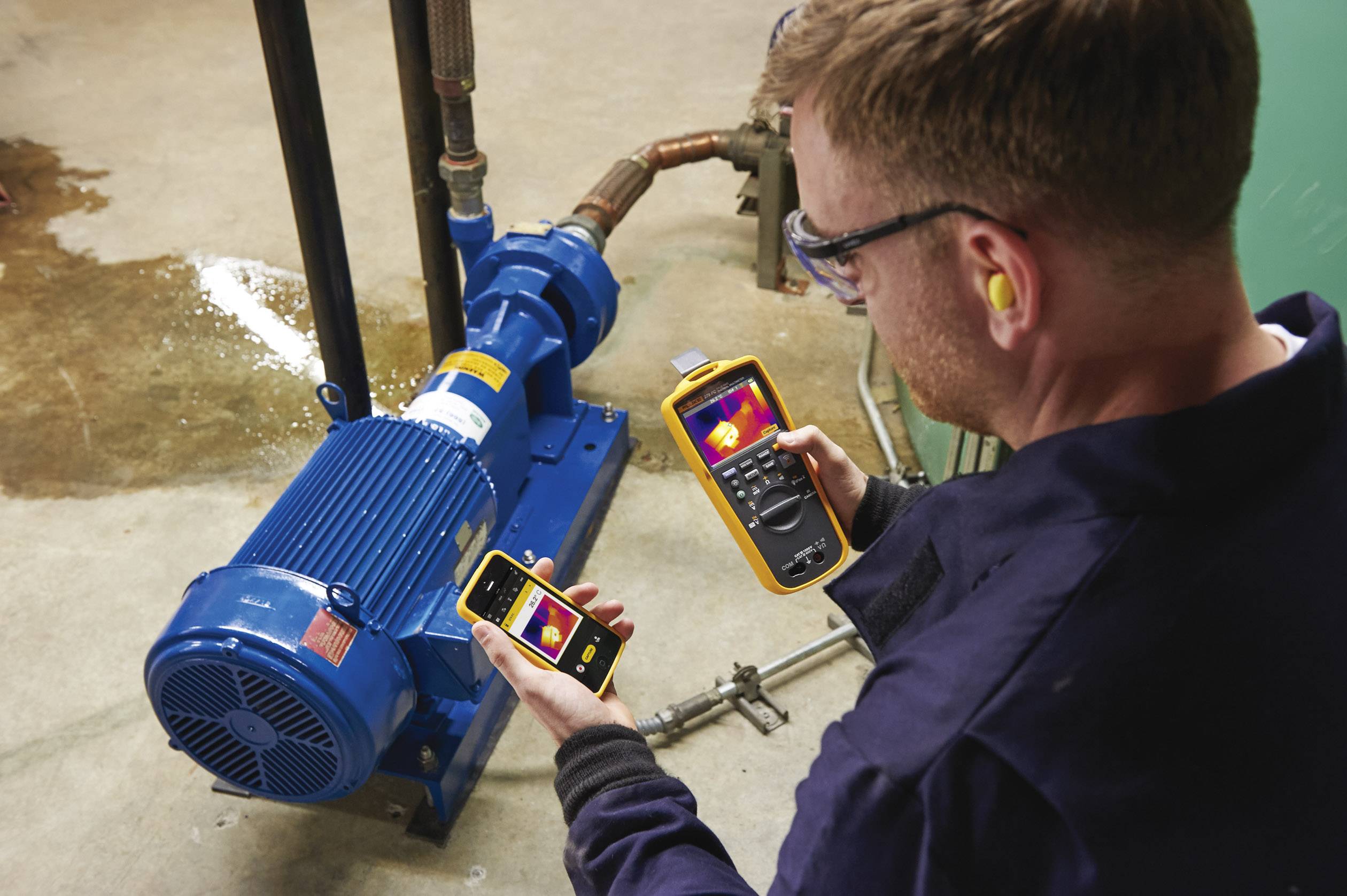 A technician is using a thermal imaging camera and a measuring device to check the temperature and functionality of an electric motor.
