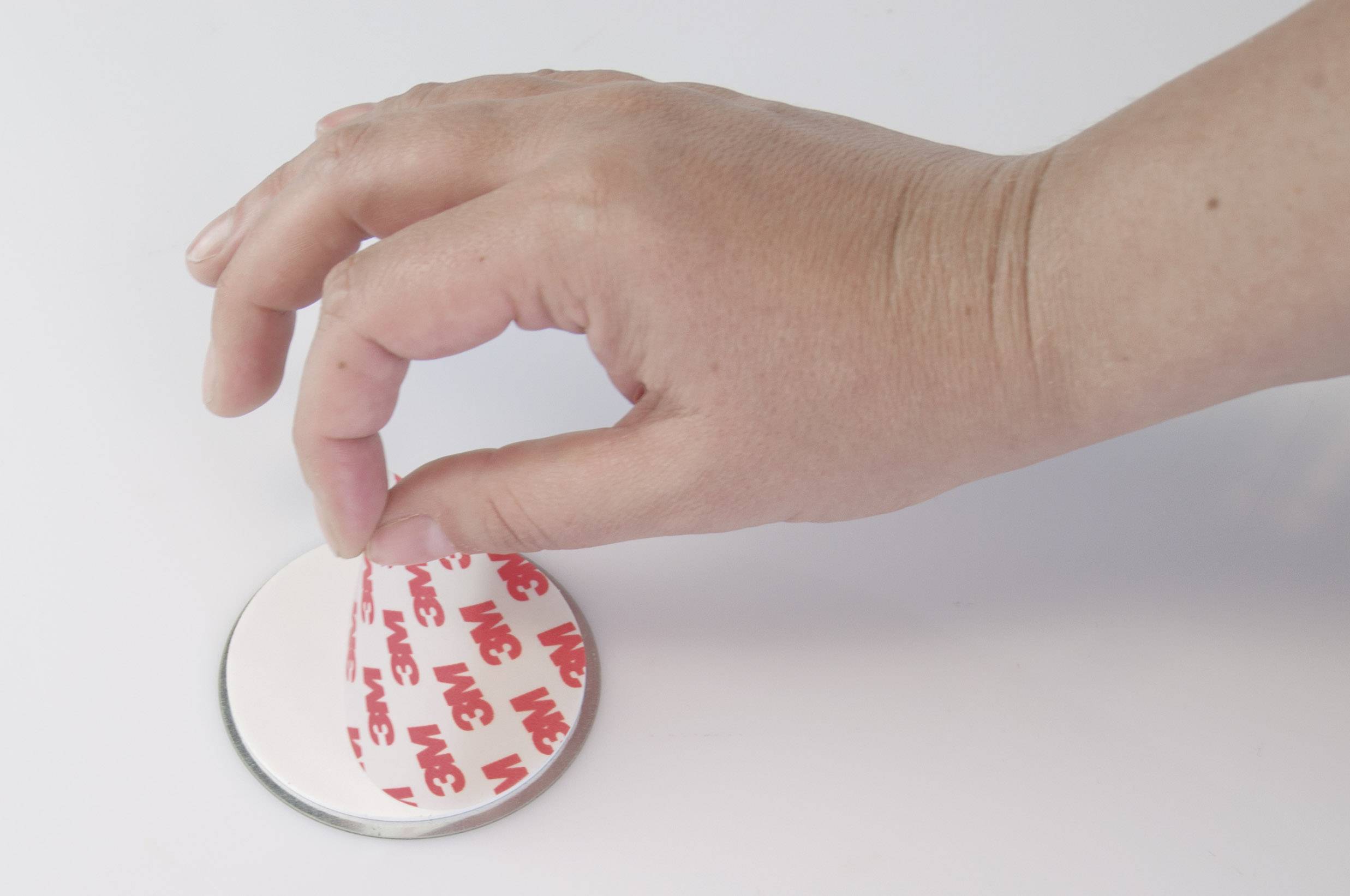 A hand peels off the protective film from a double-sided adhesive tape on a mirror.