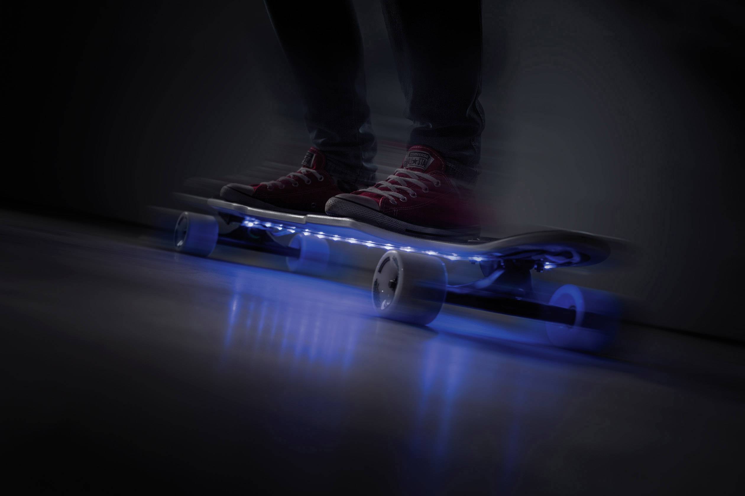 A person is riding a skateboard with blue LED lights in a dark environment, illuminating their path.