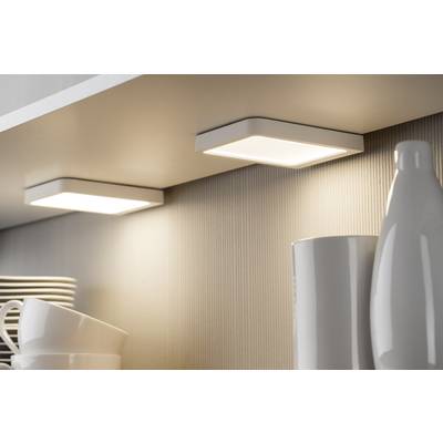 Two square LED under-cabinet lights illuminate several white cups and plates on a shelf in a modern kitchen.