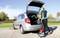 A person is cleaning the boot of a silver car with a hoover on a car park on a bright day.