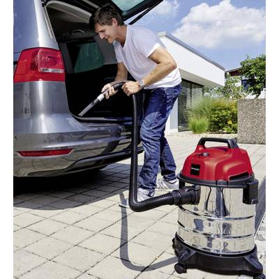 A man is cleaning the boot of his car with a wet and dry vacuum cleaner on a driveway in front of a modern house on a sunny day.
