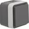 A square, grey wall switch with a white frame.