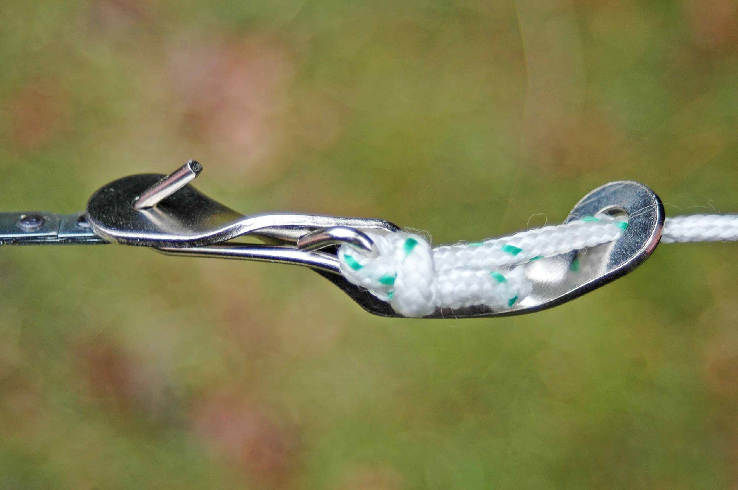 A white rope is threaded through a metal bracket that secures the rope in place. The background is blurred.