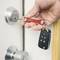 A hand is holding a key fob with a car key and inserting it into a door lock.