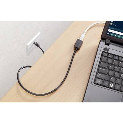 A laptop on a wooden table is connected to a wall socket via a black cable.