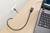 A laptop on a wooden table is connected to a wall socket via a black cable.