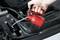 'Someone is using a red oil can to lubricate a car at the bonnet.'