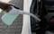 A hand is filling the windscreen washer fluid reservoir of a car with a bottle of blue liquid.