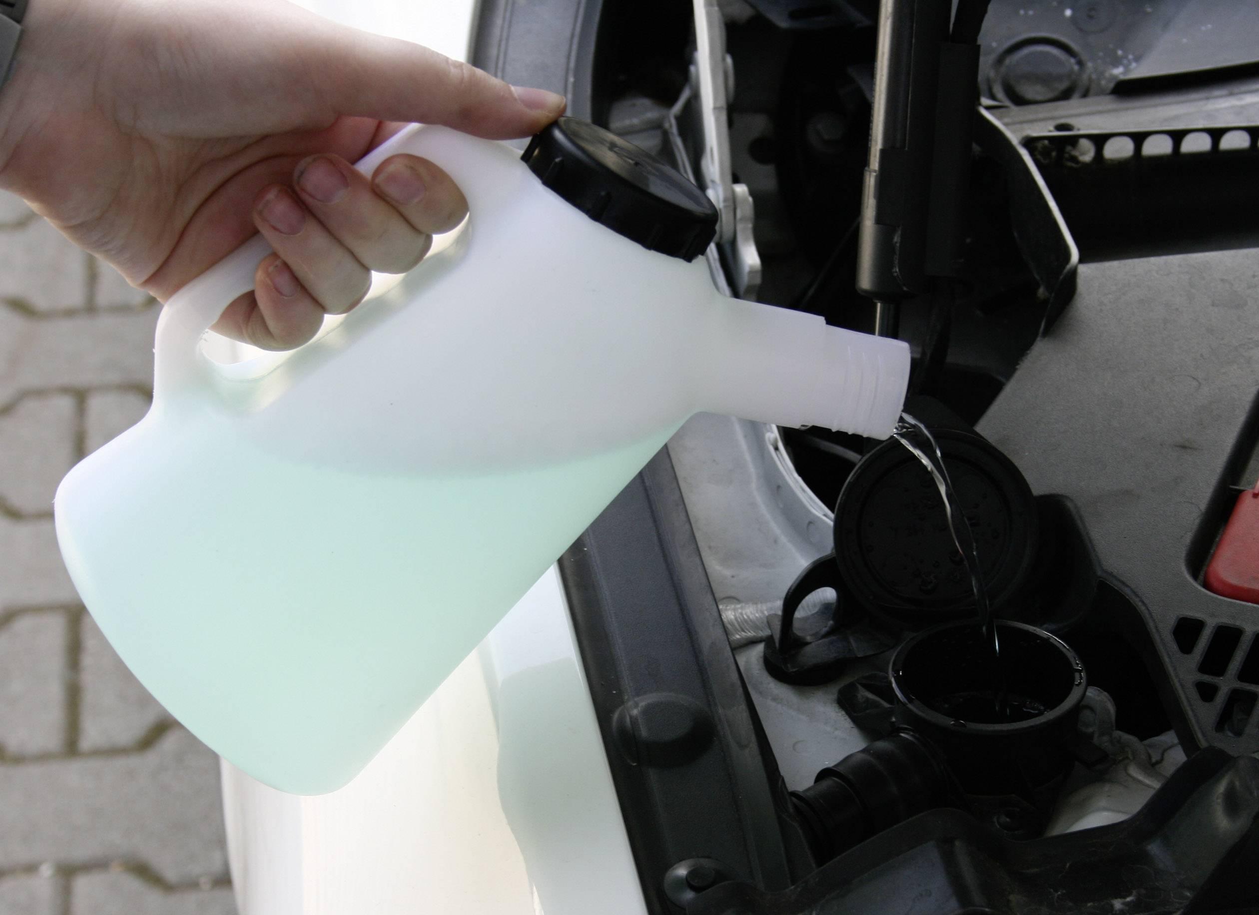 'A person is pouring coolant into a car's engine to top up the coolant level.'