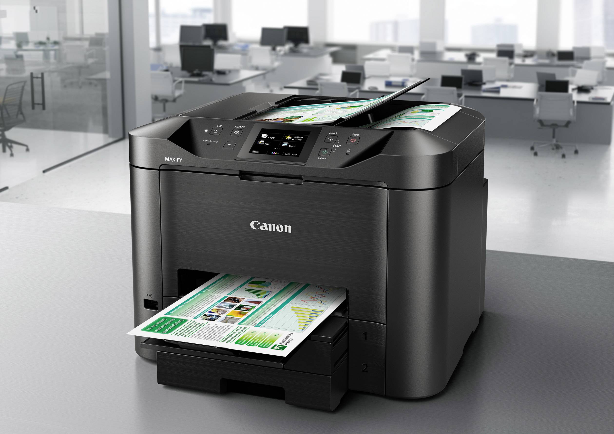 A black printer on a table in a modern office is printing colour documents with graphics and text.