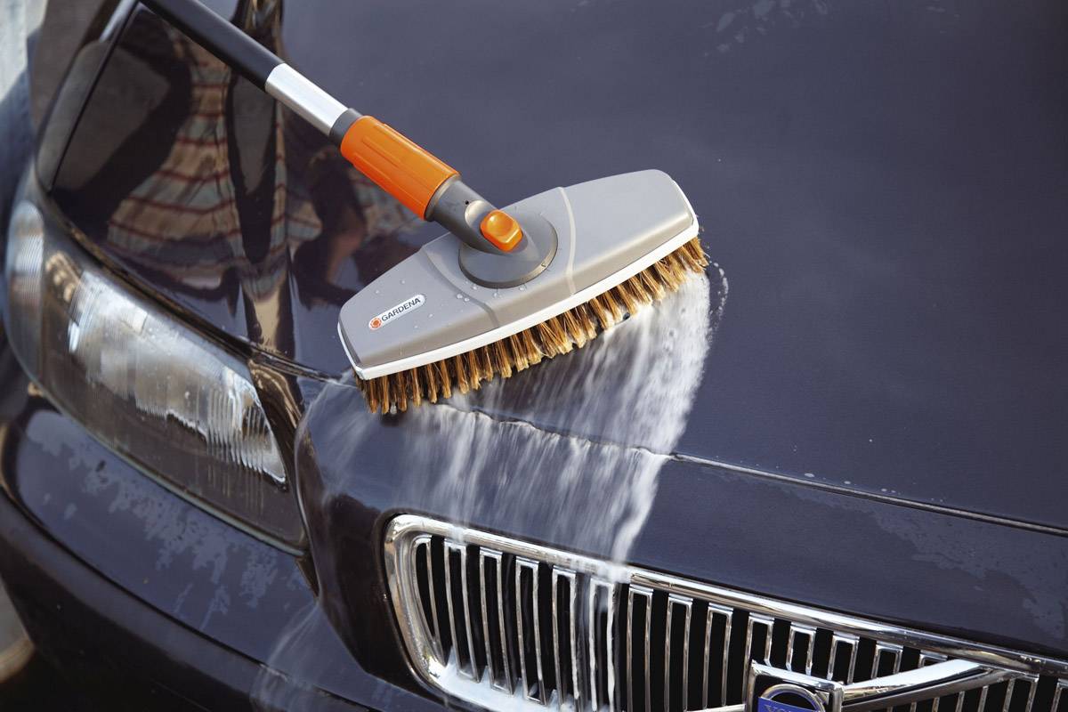 A brush is used to clean a car with water. The focus is on the cleanliness of the car's paintwork.