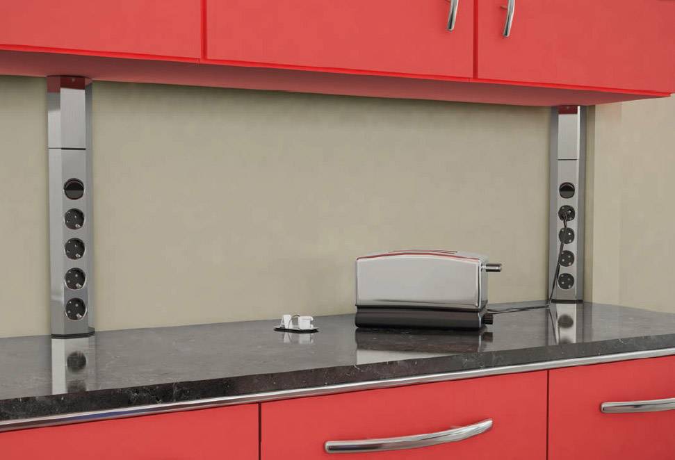 A modern kitchen with red cupboards. On the grey worktop sits a silver toaster. Plug strips are mounted on the left and right.