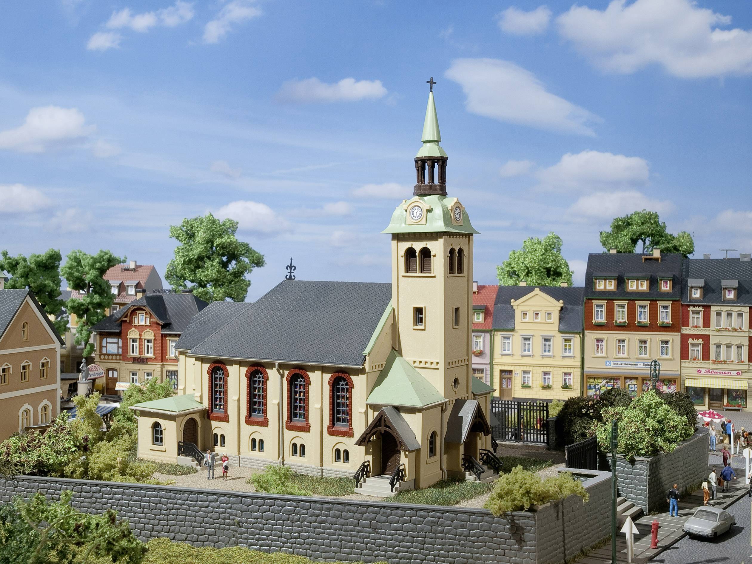 A miniature church with a green turret roof stands in the centre of a model cityscape, surrounded by colourful buildings and trees.