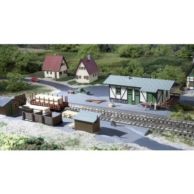 Model railway scene with a station building, track, wooden wagons, several small houses and figures in a rural setting.