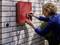A woman attaches the number '5' to a red sign on a white brick wall beside an entrance door.