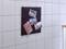 A notice board with red threads on a white tiled wall displays a postcard with 'Be my guest!' and three landscape photographs.