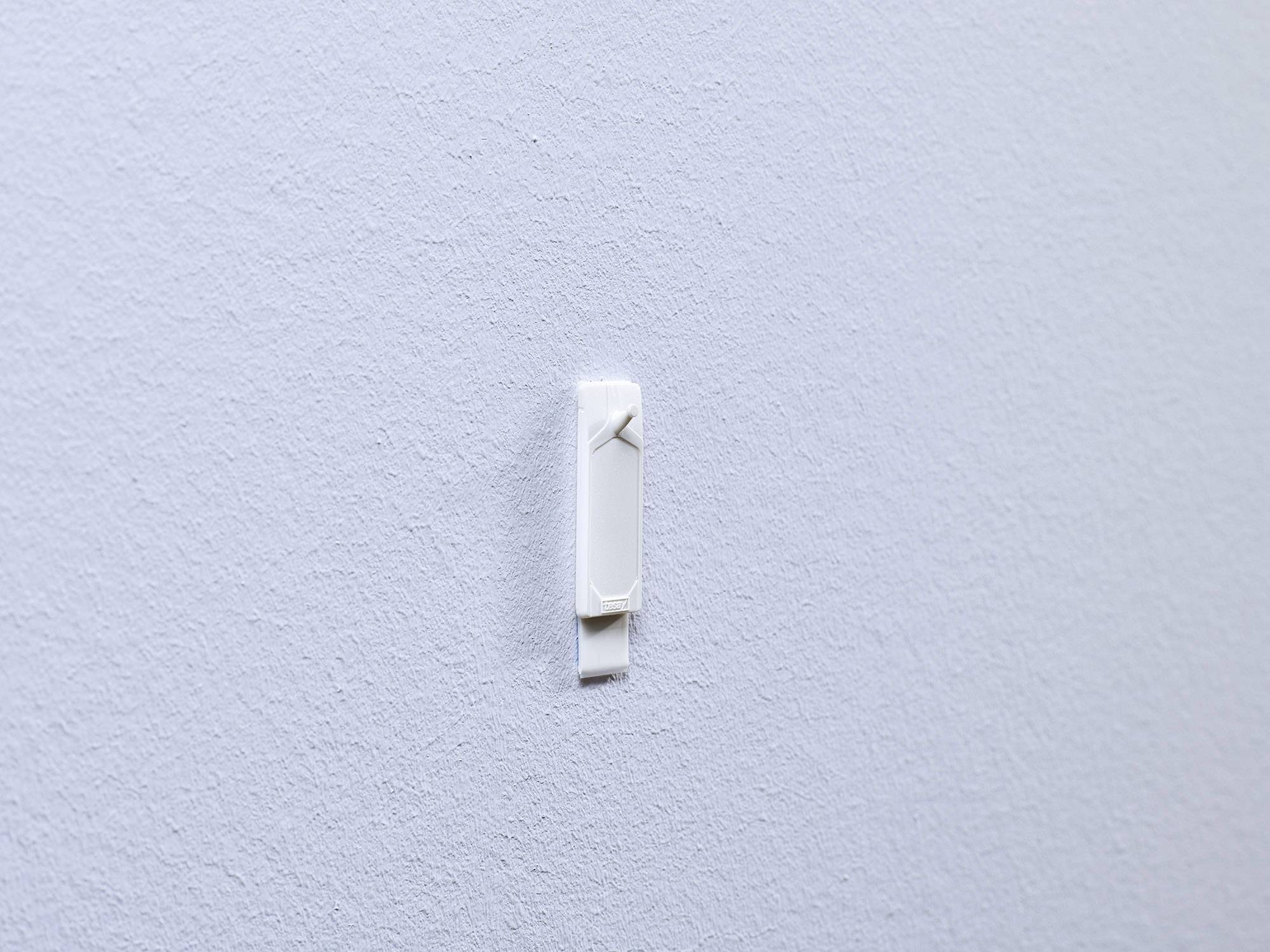 A white hook on a smooth, grey wall. The hook is empty and mounted centrally on the wall.