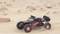 A remote-controlled car speeds across a sandy desert landscape. Large tyres kick up dust.