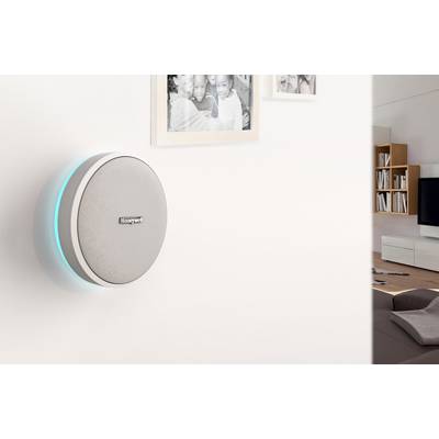 Smart thermostat on the wall of a living room, with two picture frames beside it. Living room furniture and television in the background.